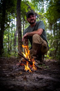 Chris Speir, founder of Speir Outdoors, gazes intently at the camera, his face illuminated by the warm glow of a campfire, set against the backdrop of the serene wilderness.